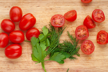 Ripe cherry tomatoes with parsley and dill in a wooden cutting board, top view