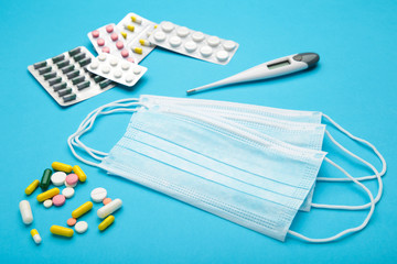 Medical thermometer and mask with pills on blue. Medical concept