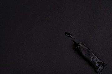 Black paint tin tube squeezed isolated on dark background. Top view.
