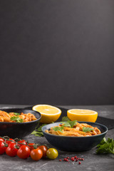 Semolina pasta with tomato pesto sauce, orange and herbs on a black concrete background. Side view, selective focus, copy space.
