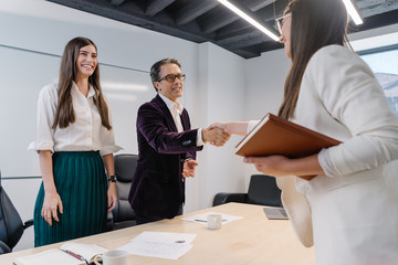 Senior human resources manager and his assistant greet job applicant with welcoming handshake and a straight smile at the job interview