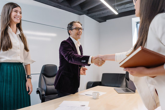 Senior human resources manager and his assistant greets job applicant with a natural smile and welcoming handshake at the job interview