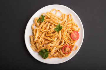 Semolina pasta with tomato pesto sauce, orange and herbs on a black background. Top view.