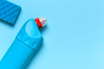Blue plastic bottle for liquid detergent, cleaning agent, bleach, antibacterial gel and washing sponge on blue background. House cleaning concept. Flat lay top view. Cleaning accessories