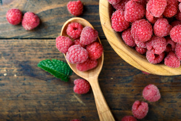 Ripe sweet raspberries in bowl on wooden table. Close up, top view.