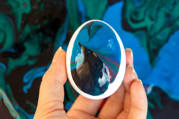 Woman hand holding half painted egg for easter. Decorating egg with glowing colours of universe