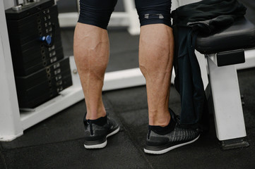 muscular calves legs of young activy athlete male wearing sneakers in sport gym