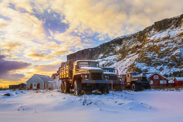 A group of three large all terrain trucks lined up surrounded by deep snow at sunrise