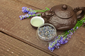 Lavender tea in a clay teapot and a clay cup with fresh and dry lavender flowers on a wooden table.