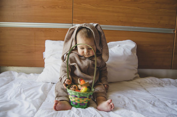 Cute baby boy in the bunny costume playing with the basket with colorful easter eggs. Easter egg...