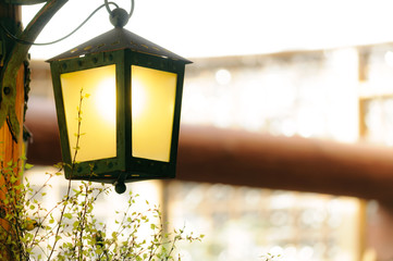 Vintage iron lantern in the interior hanging on a wooden pillar. Light is on. Spring branches of tree buds.