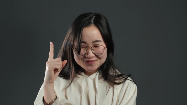 Portrait of young asian thinking pondering girl having idea moment pointing finger up on grey studio background. Smiling happy korean student showing eureka gesture.