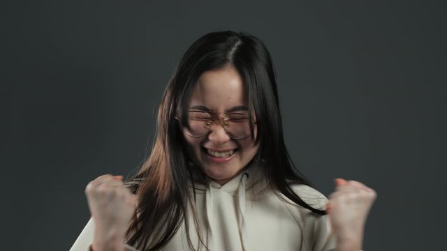 Asian girl with long hair very glad and happy, she shows yes gesture of victory, she achieved result, goals. Surprised excited happy woman on grey background