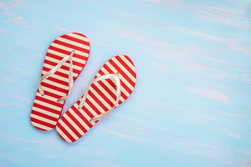 Red striped flip-flops on blue painted background, top view with copy space. Vacation time concept.