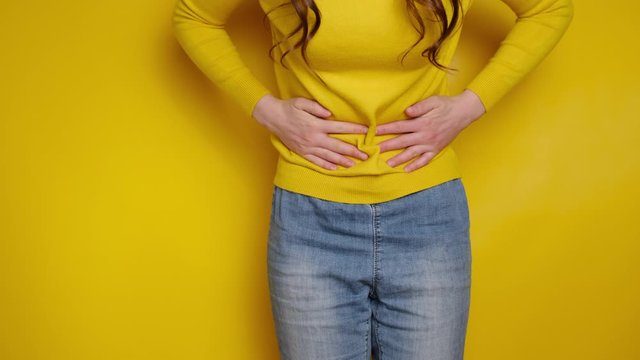 Cropped close up view girl touch stomach suffers from severe ache, keeps both hands on belly, twinges of pain caused by menstrual period, gastric ulcer, wears sweater, isolated on yellow background