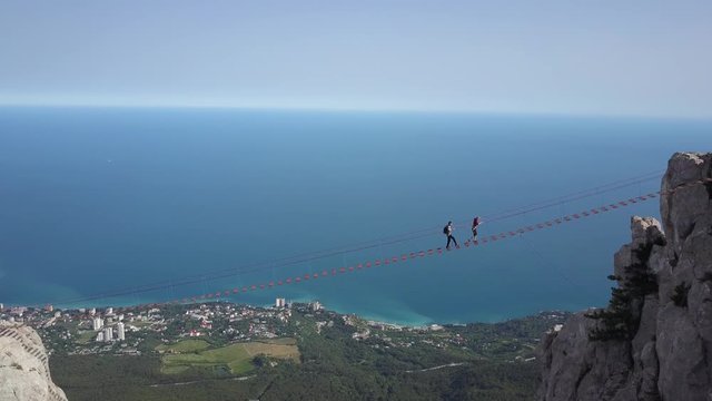 Aerial shot of tourists walking along extreme bridge to the peak of the famous Ai-Petri mountain in Crimea against the backdrop of the Black Sea and the city of Alupka, Yalta, Russia. Entertainment.