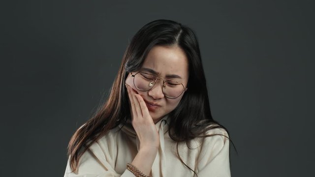 Young asian woman with tooth pain on grey studio background. Toothache, dental problems, stomatology and medicine concept.