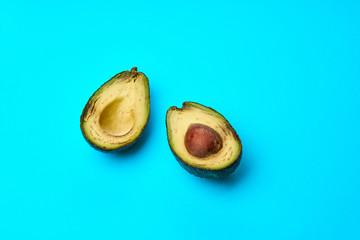A rotten avocado cut in half on blue background. One slice with core.