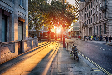 Looking towards the setting sun on Pall Mall East with bus, taxi, bicycle and people with blurred faces