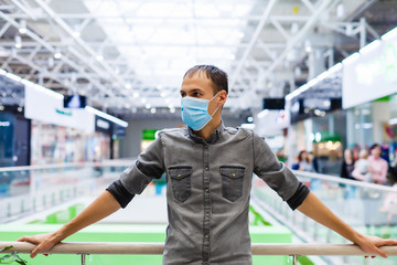 Fototapeta na wymiar A young man in a medical mask in a shopping center. The masked man protects himself from the epidemic of the Chinese virus 