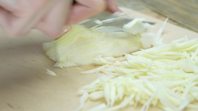 Close up of chef chopping Napa Cabbage for Asian cole slaw on a wood cutting board, selective focus. Healthy food preparation.