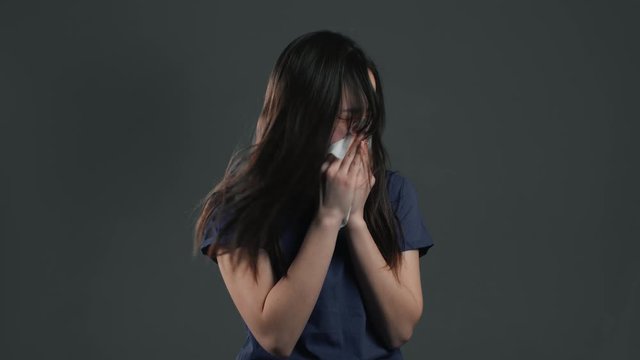 Young asian girl sneezes into tissue. Isolated woman on grey studio background is sick, has a cold or allergic reaction. Coronavirus, epidemic 2020, illness concept.