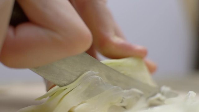 Close up of chef chopping Napa Cabbage for Asian cole slaw on a wood cutting board, selective focus. Healthy food preparation.