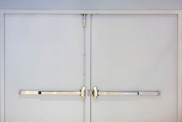 Emergency fire exit door. Closed up latch and rusty door handle of emergency exit. Push bar and rail for panic exit. Open one way door.  steel of handle for the white door fire exit