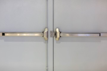 Emergency fire exit door. Closed up latch and rusty door handle of emergency exit. Push bar and rail for panic exit. Open one way door.  steel of handle for the white door fire exit