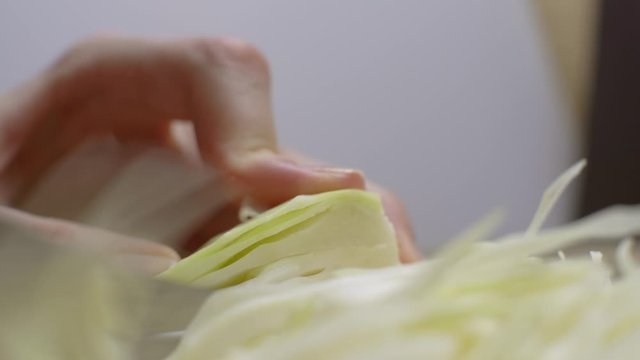 Close up of chef chopping Napa Cabbage for Asian cole slaw on a wood cutting board, selective focus. Healthy food preparation.
