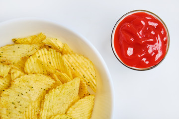 Fluted chips in a white plate next to ketchup. Top view.