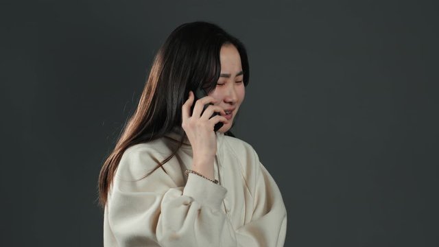 Woman with asian appearance sort things out, swears with somebody by mobile phone. Girl nervous, expresses discontent and resentment.