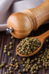 green peppercorns in wooden scoop on rustic background