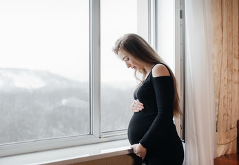 Fototapeta premium A pregnant girl is breathing fresh air from the window
