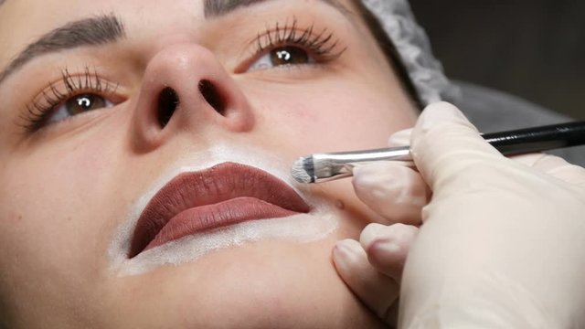 Microblading, micropigmentation lips work flow in a beauty salon. Woman having lip drawn and tinted with pencil, preparing for semi-permanent makeup.