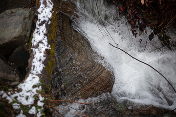 A mountain river flows over stones. River in the mountains in winter. A stream of water along a rocky slope. Clear water from a glacier flows along a rocky bottom.