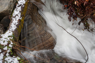 A mountain river flows over stones. River in the mountains in winter. A stream of water along a rocky slope. Clear water from a glacier flows along a rocky bottom.