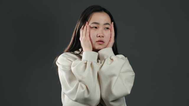 Frustrated bored asian girl over grey wall background. Woman is tired of work or studying, she disappointed, helpless