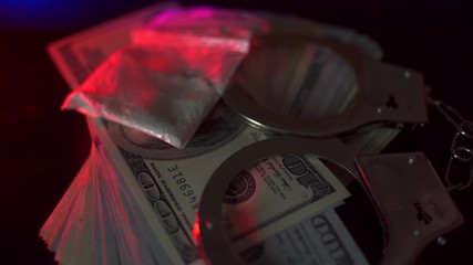 police flasher.. Handcuffs, drugs and a lot of money are on the table. They are illuminated by a police flasher glowing in red and blue. - Powered by Adobe