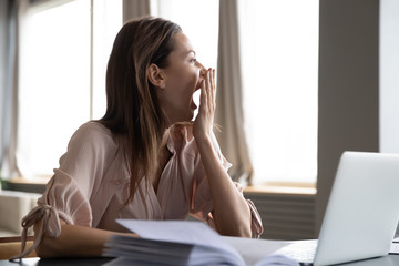 Head shot distracted from work study young woman yawning, having lack of energy during workday at...