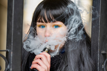 Vape teenager. Young pretty white caucasian brunette girl with blue eyes and in a blue jacket...