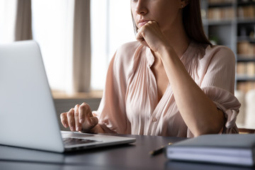 Close up cropped image thoughtful young woman propping head with hand, looking at computer screen....