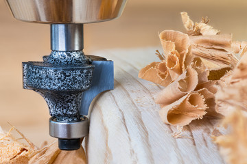 Shaping copying shank router bit clamped in chuck of a working machine tool. Sharp steel woodworking milling cutter with bearing forming a round edge on wood plank. Pile of twisted shavings. Joinery. - obrazy, fototapety, plakaty