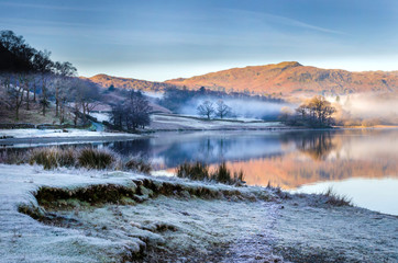 A morning scene with reflections of the frost and mist lifting from Grasmere lake in the Lake...