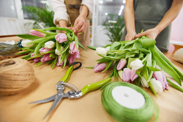 Obraz premium Close up of two unrecognizable young women arranging tulip bouquets and floral compositions for Spring season while working in flower shop, copy space