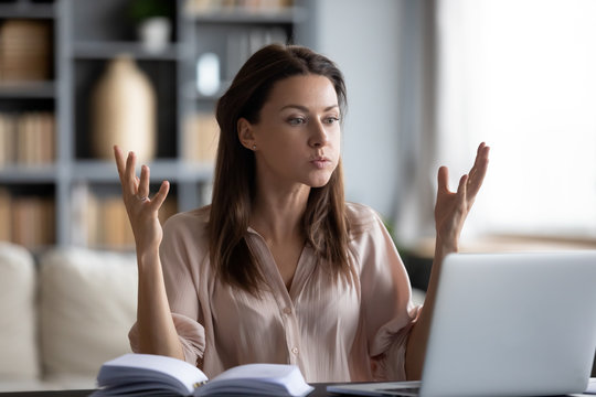 Unhappy young woman looking at laptop screen, irritated by bad gadget work, low internet connection, working remotely at home. Stressed attractive lady annoyed by hard work task or system crash.