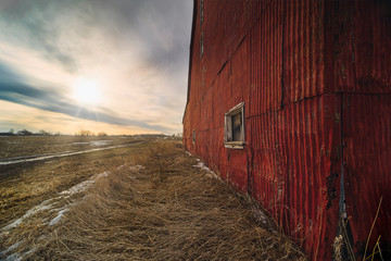 Stunning dramatic sunsets in rural farm country with barns and cold fields with rainbow.