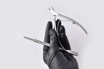 hand in a black protective glove holds manicure and pedicure tools on a white background