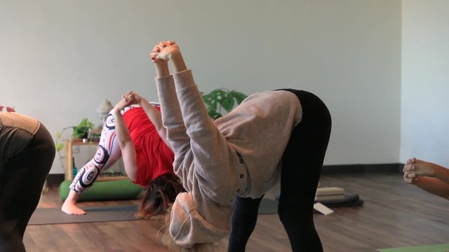 Group of woman practicing prasarita padottanasana bend with hand rotation on back towards spine while standing on yoga mat