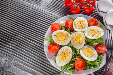 salad with boiled chicken eggs and cherry tomatoes on a wooden rustic background